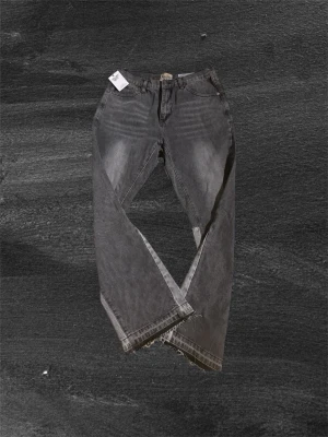 Grå jeans från Gallery Dept. - Säljer ett par grå jeans från Gallery Dept. med coolt slitna och fransiga benslut. Jeansen har klassisk femficksdesign och raka ben. Materialet är robust denim och färgen är mörkgrå med tvättade detaljer för en vintagekänsla. Perfekt för dig som gillar streetwear och unik stil.