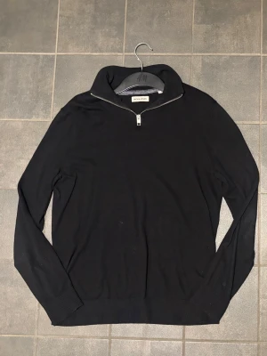 Svart half zip tröja Jack & Jones - Svart långärmad tröja från Jack & Jones med stilren half zip-dragkedja i halsen. Tröjan har ribbade muddar och är gjord i mjukt material som känns skönt mot huden. Perfekt för dig som gillar enkel och clean stil.