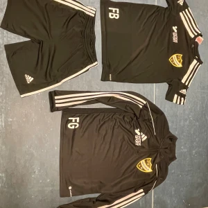 Träningsställ Adidas - Träningsställ från Adidas, inklusive shorts, t-shirt och långärmad tröja. Klubbemblem och initialer på tröjorna. 