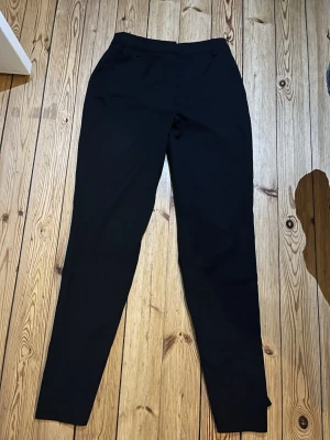 Svarta kostymbyxor från Bik Bok - Snygga svarta kostymbyxor från Bik Bok i klassisk rak modell. Byxorna har midwaist, bälteshällor och sidfickor. Materialet är mjukt och känns bekvämt mot huden, perfekt för en clean och stilren look.