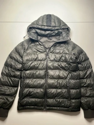 Peak Performance dunjacka - Säljer en jättefin mörkgrön dunjacka från Peak Performance. Jackan är både praktisk och snygg. Den har dragkedja, fickor, huva och logotyp på ärm och bröst. Går att styla till allt, är väldigt behaglig och håller en varm. Jackan är värderad till ett nypris på 2100 kr. Jackan har två små revor som är snyggt lagade hos en skräddare. Utöver revorna har jackan ett mycket bra skick. Priset är inte hugget i sten!