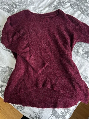 Vinröd stickad tröja med lång ärm - Vinröd stickad tröja med lång ärm och rund hals. Tröjan har en lös passform och är tillverkad i ett fluffigt stickat material. Storlek S, kan även passa M.