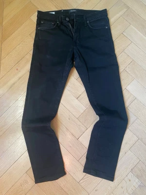 Svarta skinny jeans från Jack & Jones - Svarta jeans från Jack & Jones i modellen Glenn med skinny fit. Klassisk femficksdesign, dragkedja och knapp i midjan. Jeansen är tillverkade i stretchig bomull för en bekväm passform och har en smal siluett som sitter snyggt längs benen.
