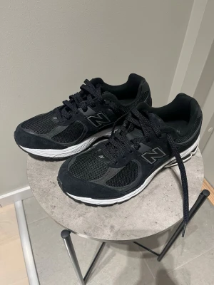 Svarta New Balance sneakers - Säljer ett par svarta New Balance sneakers med vit sula och meshdetaljer. Skorna har snörning och en rund tå, med snygga New Balance-loggor på sidorna. Ovandelen är i mesh och mocka för både stil och komfort. Perfekta för dig som gillar sportig och clean look