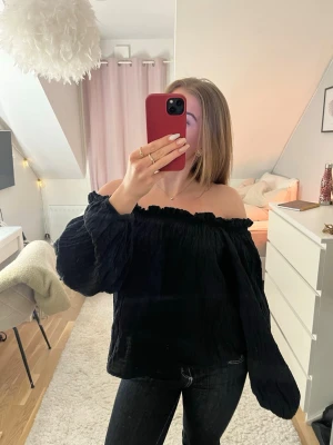 GINA-Svart offshoulder blus med volymärmar - Säljer en svart blus med offshoulder-modell från Gina Tricot. Blusen har en rynkad, elastisk kant upptill. Denna topp är perfekt att styla med jeans eller kjol. Säljs pga används aldrig🌺