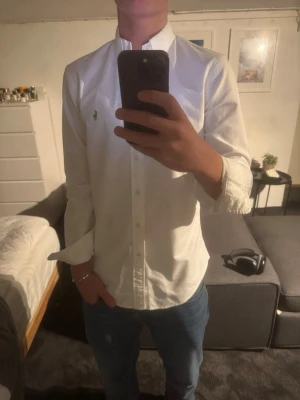 Vit skjorta från Polo Ralph Lauren - Klassisk vit skjorta från Polo Ralph Lauren i slim fit. Skjortan har button-down krage, broderad logga på bröstet och knappar hela vägen. Tillverkad i mjuk bomull och har långa ärmar. Perfekt till jeans eller chinos för en clean look.
