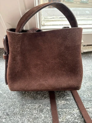 Brun mocka axelväska från ARKET - Säljer denna väska ifrån Arket som är i jättefint skick. Väskan har använts ett fåtal gånger men kommer tyvärr inte till användning längre. Nypris 1390kr. Skriv vid frågor💗