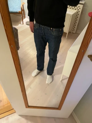 Levi's 501 jeans  - Säljer ett par klassiska Levi's 501 jeans i mörkblå tvätt med straight fit. Jeansen har fem fickor, knappgylf och den ikoniska läderpatchen bak i midjan. Materialet är slitstarkt denim i bomull och passformen är normal med raka ben. Mycket bra skick. Priset ej hugget i sten.