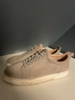 Beige sneakers från Louboutin - Snygga beige sneakers från Louboutin med klassisk röd sula och platt vit sula. Skorna har rund tå, snörning och är tillverkade i mocka med diskreta detaljer. Perfekt för dig som gillar stilrena och exklusiva sneakers med en twist. Ingen låda ingår utan bara skor och en påse. Säljer också för ett så billigt pris eftersom ett styng på flärpen i bak har gått av vilket går att sy ihop. Dom är också ganska smutsiga så det är också en anledning av det billiga priset. Hör av dig om du undrar något😁