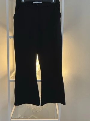 Svarta bootcut-byxor från 157 - Svarta bootcut-byxor från 157 i storlek S. Byxorna har en klassisk knappstängning och är tillverkade i ett mjukt tyg som ger en snygg siluett. Perfekta för dig som gillar stilrena och trendiga plagg med lite vidare ben.