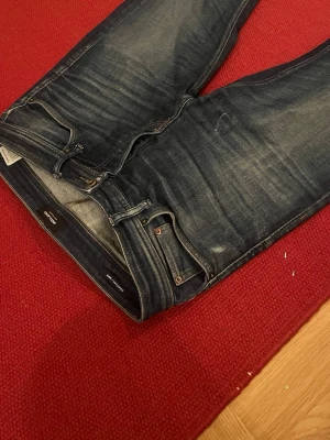 Jack and Jones - Säljer ett par mörkblå tapered jeans från Jack & Jones med snygga slitningar. Rak passform hela vägen ner. Strlk 32/34
