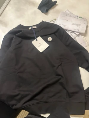 Moncler hoodie - Svart sweatshirt från Moncler med rund hals och Moncler-logga på bröstet. Tröjan har långa ärmar med ribbade muddar och är tillverkad i mjuk bomull. Perfekt för dig som gillar stilrena och exklusiva märken. Den passar också xl gå ner i snabb affär 