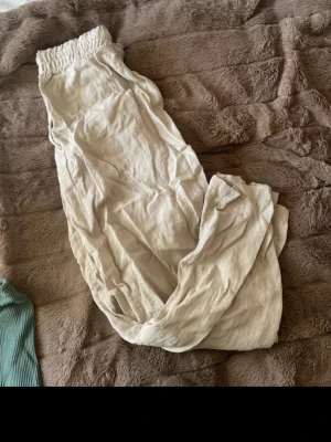 Beiga linnebyxor med snörning från H&M - Säljer ett par beiga linnebyxor från H&M i storlek M. Byxorna har elastisk midja och snörning med repdetalj. Materialet är linneblandning som ger en skön och luftig känsla. Perfekta för chill dagar och sommarhäng.
