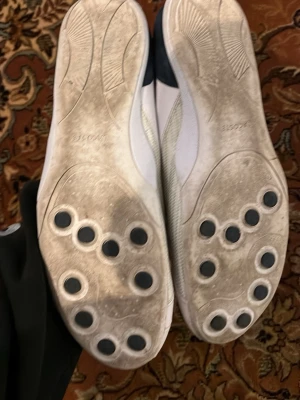 Vita sneakers från Lacoste med kardborre - Säljer ett par vita sneakers från Lacoste med kardborrestängning och meshdetaljer på sidorna. Skorna har rund tå, platt sula med svarta gummipluppar undertill och diskret Lacoste-logga på sidan. Tillverkade i skinn och syntet, insida i mörkblått tyg.