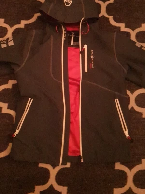 Ljusblå vindjacka Sail Racing XS - Hej min sail racing jacka är xs men passar på m. Jjusblåvindjacka från Sail Racing i storlek XS med vit dragkedja och röda meshdetaljer på insidan. Jackan har huva, flera fickor med dragkedja och snygga logoprints på bröstet och ärmen. Perfekt för dig som gillar sportig och clean stil.