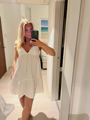 Vit kort sommarklänning Zara - Superfin vit kort klänning med v-ringad hals och volangkant nertill. Klänningen är ärmlös med smala axelband och har en luftig, flowy passform som är perfekt för varma dagar. Tillverkad i ett lätt bomullstyg som känns skönt mot huden.