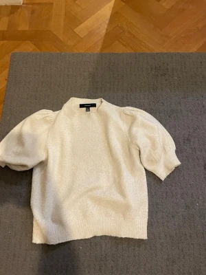 Krämvit puffärm tröja H&M - Säljer en krämvit tröja från H&M med puffärmar och ribbade muddar. Tröjan har en mjuk, lite fluffig struktur och kortare ärmar som ger en trendig look. Perfekt att styla med jeans eller kjol för en cool vardagsoutfit. Köpte den för 400-300