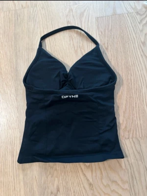 Svart linnetopp från DFYNE - Snygg svart linnetopp från DFYNE med halterneck och lätt rynkning vid bysten. Toppen har en enkel och sportig look, perfekt till träning eller chill outfits. Mjukt och stretchigt material som sitter skönt på kroppen.
