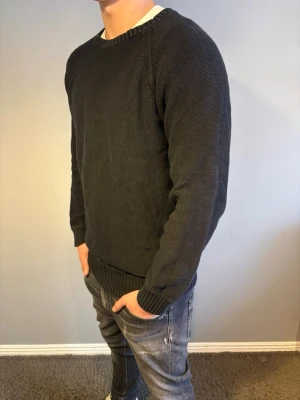 Svart stickad tröja  - Snygg svart stickad tröja med rund halsringning och ribbade muddar vid ärmslut och nederkant. Storlek M. Modellen är 184cm