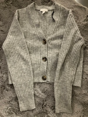 Jättefin Grå stickad kofta! - Jättegullig grå stickad kofta med stora knappar, och V ringad. Den är använd någon gång. Den har ett ribbat mönster.