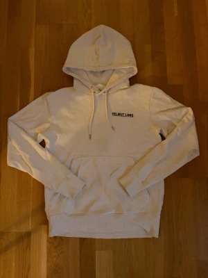 Vit hoodie från Helmut Lang - Säljer en stilren vit hoodie från Helmut Lang med klassisk huva och dragsnören. Skick 7/10 bra skick förutom en fläck på armbågen därav det billigare priset. Syns dock inte så mycket vid användning. Pris är ej hugget i sten!