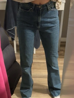 Blå bootcut jeans med hög midja - Säljer ett par klassiska blå jeans med bootcut och hög midja. Jeansen har fem fickor, knappgylf och är tillverkade i ett tåligt denimtyg. Perfekta för dig som gillar en tidlös och avslappnad stil. Säljer då dem är för stora för mig. Modellen tall från asos, avklippta nertill men passar 172cm