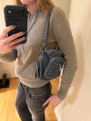 Blå mocka axelväska med nitar - Säljer en blå väska från noella! Avtagbar axelrem så man kan välja mellan att ha den på axlen eller runt midjan 