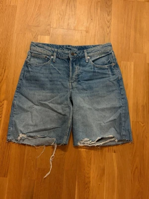 Blå denimshorts från Weekday - Säljer ett par blå denimshorts från H&M med fransiga kanter och slitningar nere. 