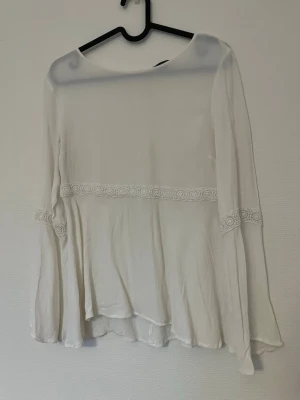 Vit blus med spetsdetaljer - Vit blus med spetsdetaljer och utsvängda armar och nedtill på tröjan, lite genomskinlig.