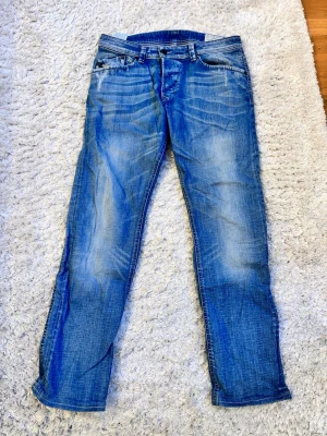 Blå Diesel Darron jeans W30 L32 - Säljer ett par blå Diesel Darron jeans med snygg tvätt och slitningar. Modellen är regular slim-tapered och har klassiska fem fickor samt Diesel Industry-detalj på myntfickan. Jeansen är tillverkade i stretchigt denim för extra komfort.
