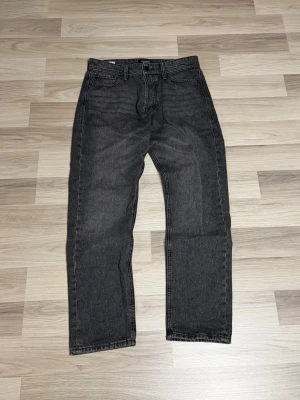 Mörkgråa jeans från Jack & Jones - Klassiska mörkgråa Jack & Jones jeans med rak passform och fem fickor. Jeansen har en tidlös look med normal midja och är tillverkade i slitstarkt denimtyg. Perfekta för dig som gillar en enkel och clean stil.