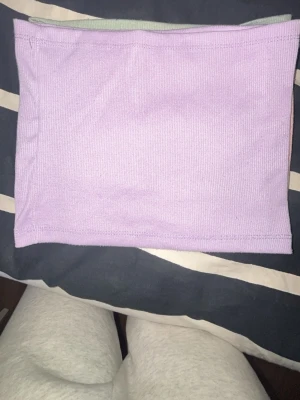 Ljuslila bandeau tubtopp - En enkel och stilren ljuslila bandeau tubtopp i ribbad bomull. Perfekt att matcha med höga jeans eller kjol för en trendig look. Toppen är ärmlös och har en mjuk, stretchig passform.