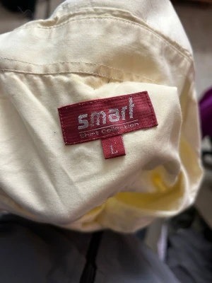 Ljusgul kortärmad skjorta Smart - Kortärmad skjorta från Smart Shirt Collection i en ljusgul färg. Klassisk krage, bröstficka och knäppning framtill. Tillverkad i ett tunt och mjukt bomullstyg som passar perfekt till varmare dagar. Enkel och stilren design. skjortan har några fläckar på sig