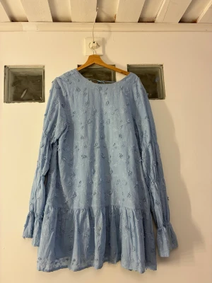 Klänning -nakd - Ljusblå broderad klänning från NA-KD – stl 42 – mycket fint skick  Vacker ljusblå klänning från NA-KD med broderade blommor och volangkjol. Långärmad modell i luftigt och mjukt tyg, med djupare rygg och knytning baktill. Använd endast 1 gång, i mycket bra skick, inga fläckar eller skador.