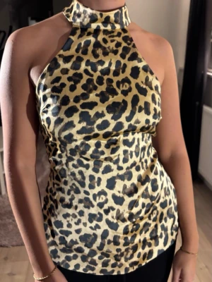 Leopardmönstrad halterneck topp - Snygg leopardmönstrad halterneck topp med hög krage och öppen rygg. Toppen knyts i nacken och bak, vilket ger en unik och trendig look. Perfekt för dig som vill sticka ut och älskar djurmönster.