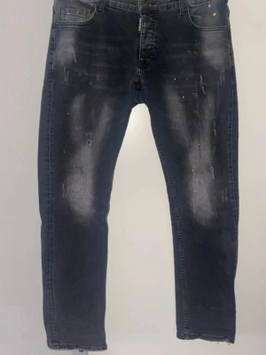 ***Dsqured2 jeans*** - Snygga mörkgrå jeans med slitningar och färgstänk i blått och rött. Jeansen har en rak passform och klassisk femficksdesign.
