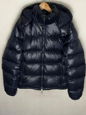 Mörkblå dunjacka från Ralph Lauren - Snygg mörkblå puffer dunjacka från Ralph Lauren med hög krage och dragkedja framtill. Jackan har två sidofickor med dragkedja och en quiltad design som ger en modern look. Perfekt för kalla dagar och enkel att matcha med olika outfits. Priset är ej hugget i sten