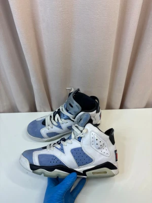 Nike Air Jordan 6  - Nike Air Jordan 6 sneakers i blått och vitt med svarta detaljer. Skorna har hög siluett, snörning och perforerade paneler. Ikonisk Jumpman-logga på hälen och en platt sula. Tillverkade i skinn och syntetmaterial.