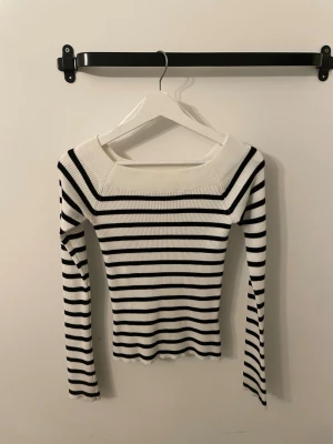 Randig ribbad långärmad topp - Säljer en vit och svart ribbad topp med lång ärm och bred, fyrkantig ringning. Toppen har ett tight passform och klassiskt randigt mönster som ger en stilren look. Perfekt att matcha med jeans eller kjol för en trendig outfit.