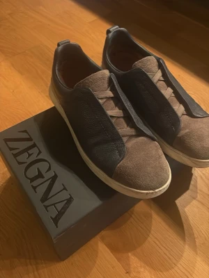 Zegna Triple Stitch Skor - Säljer ett par Zegna Triple Stitch sneakers i brun mocka med marinblåa skinnpaneler. Riktigt stilrena, köpta i Zegna Butiken vid Dubai mall för ca 9400kr nypris med en rabbat. Riktigt gott skick, kan tvättas innan frakt. Hör av dig för fler bilder eller funderingar
