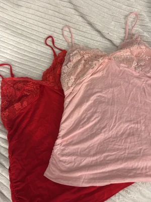 Två spetsnattlinnen i rött och rosa - Säljer två nattlinnen med tunna axelband, ett i rött och ett i ljusrosa. Båda har spetsdetaljer upptill och är gjorda i ett mjukt, stretchigt material.