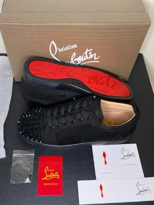  Christian Louboutin skor  - Säljer ett par svarta sneakers från Christian Louboutin med ikoniska röda sulor och svarta nitar på tån. Skorna har snörning och är tillverkade i mocka och skinn, vilket ger en lyxig och edgy vibe. Perfekta för dig som vill sticka ut med din stil.