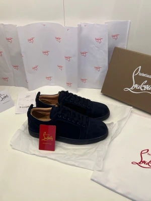Mörkblå sammetssneakers Louboutin - Snygga mörkblå sneakers från Christian Louboutin i mjuk sammet med ton-i-ton broderad logga på hälen. Klassisk låg modell med rund tå, snörning och svart platt sula. Perfekta för dig som vill ha en exklusiv och stilren look.