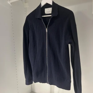 Mörkblå stickad kofta från Jack & Jones - Säljer en mörkblå stickad kofta med hel dragkedja framtill och klassisk krage. Tröjan är använd en gång och är då i riktigt bra skick. Storleken är konstig då det står XS men passar S/M med, 