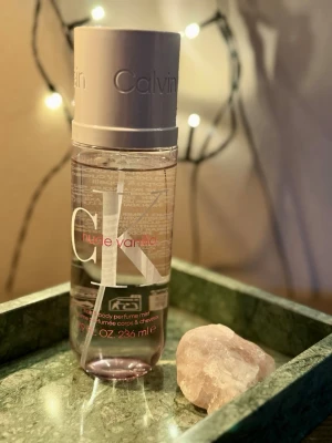 CK Nude Vanilla Body Perfume Mist - Fräsch body perfume mist från Calvin Klein i doften Nude Vanilla. Flaskan är genomskinlig med vit kork och har en modern, stilren design med stora CK-bokstäver och rosa detaljer. Innehåller 236 ml och passar perfekt för dig som gillar lätta, söta dofter.