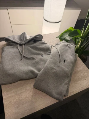 Ralph Lauren tracksuit - Säljer ett stilrent Polo Ralph Lauren sett med klassisk huva och dragsnören och sköna byxor. De har den ikoniska lilla broderade loggan och är gjord i mjukt bomullsmaterial. Perfekt för en avslappnad och trendig look.