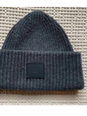 Mörkgrå ribbstickad mössa Acne Studios - Säljer en mörkgrå ribbstickad mössa från Acne Studios med den klassiska ansiktsloggan framtill💕💕💕