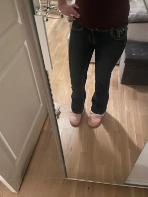 Blå bootcut jeans med detaljer - Säljer ett par snygga blå bootcut jeans med dekorativa fickor bak med knappar. Jeansen har låg midja och klassisk femficksdesign. 