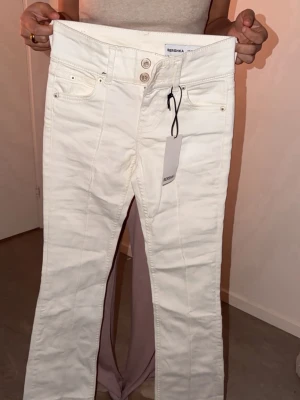 Vita low waist  jeans från Bershka - Snygga vita jeans från Bershka med low midja och raka ben. Jeansen har dubbla knappar i midjan, fem fickor och markerade sömmar framtill. Tillverkade i ett stretchigt denimtyg för skön passform. Perfekta för en clean och trendig look.