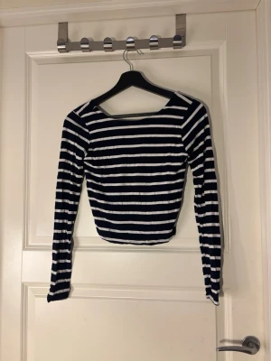 Randig croppad topp med lång ärm - Snygg croppad topp med marinblå och vita ränder. Toppen har långa ärmar och en bred, rund ringning fram samt rundad rygg. Perfekt till jeans eller kjol för en trendig look.